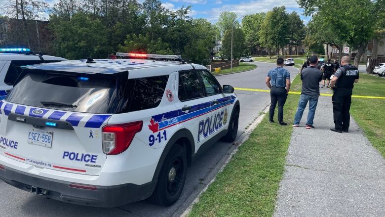 Residents and police stand next to a crime scene surrounded by police tape in a residential neighbourhood.