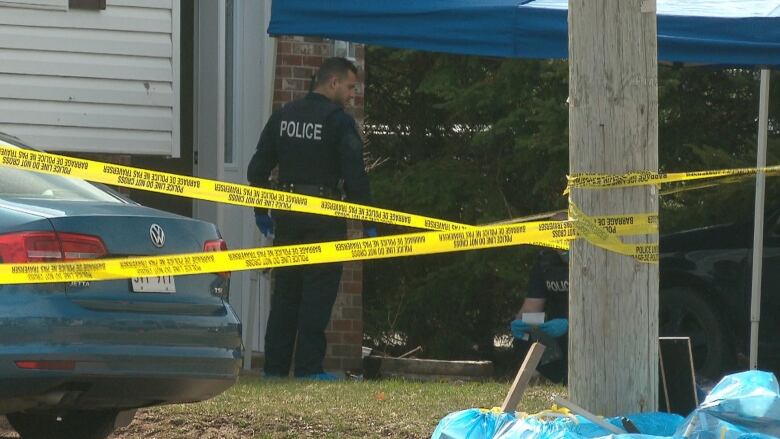 Crisscrossed yellow police tape in the foreground with police officers in the background.