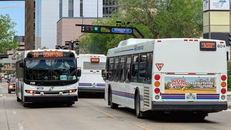 A bus that says 66 Downtown on the front display drives toward the camera, passing busses driving in the opposite direction.