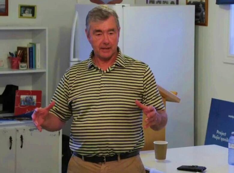 A man wearing a striped green short-sleeved shirt addresses a meeting at a community centre