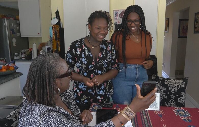 A woman holds up a phone as two teens look into it smiling.