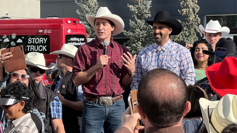 two men in cowboy hats and jeans speak to a crowd