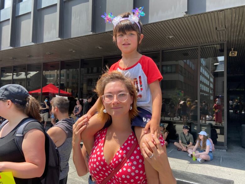 A mother in a red polka dotted dress stands with a small boy on her shoulders.