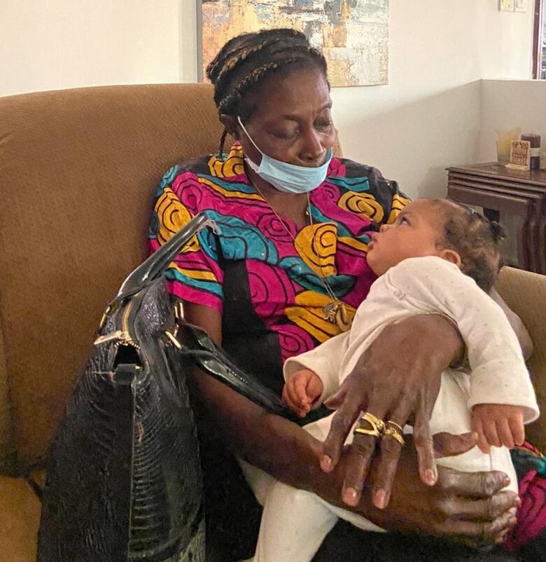 A woman holds a baby while sitting on a couch.