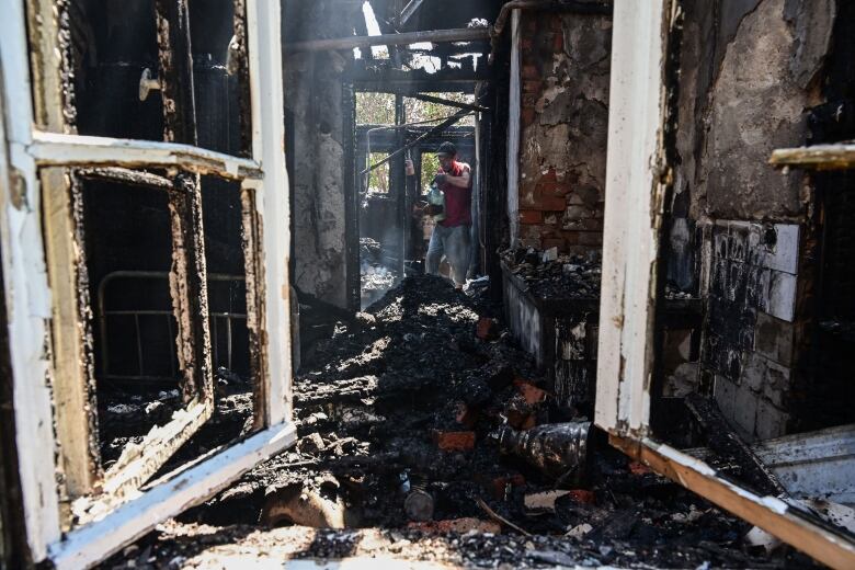 A man in a baseball cap and red shirt holds up a fire extinguisher in a burned-out structure.