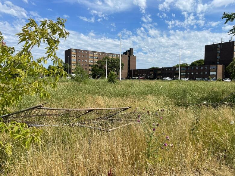 A fence lays partially destroyed in the grass in front of a large apartment building. 