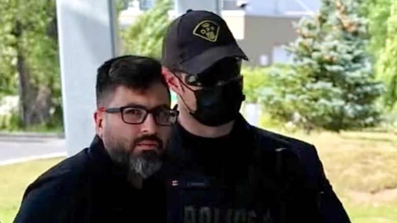 A man looking at the camera, surrounded by police.