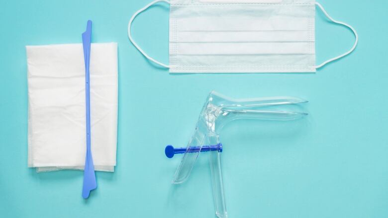 An overhead photo of the vaginal speculum, napkin, surgical mask, and cervical spatula used to collect Pap test specimens. 