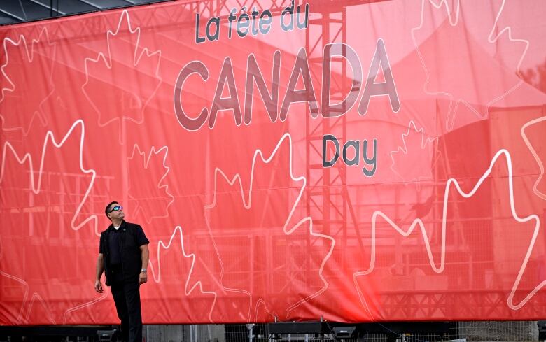 A security worker looks up at a big red 'Canada Day' sign.