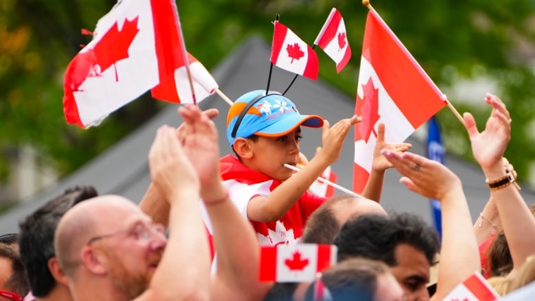 People, including a child with a Canada flag headband, wave flags and cheer.