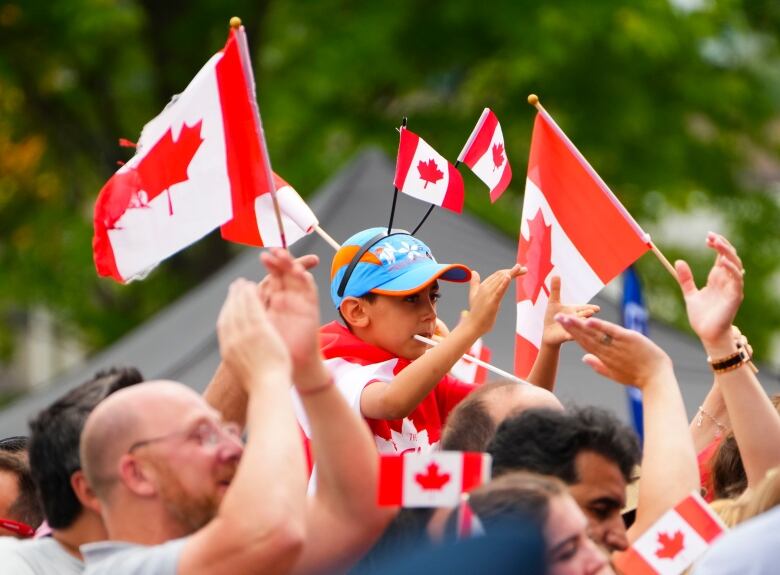 People, including a child with a Canada flag headband, wave flags and cheer.