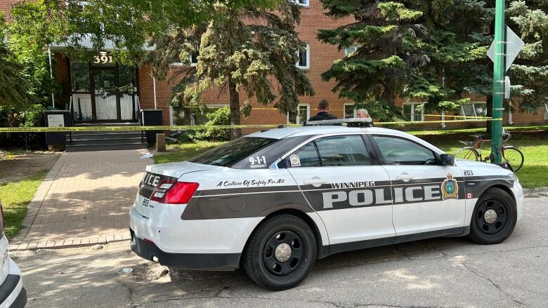 A police car sits in front of a building cordoned off with yellow tape.