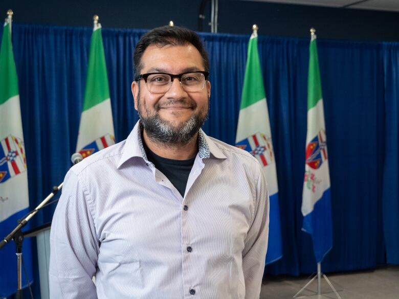 A portrait of a man smiling with flags behind him.