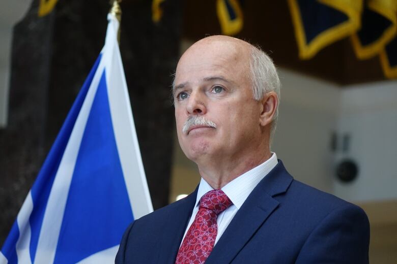 A man stands at the microphone during a press conference. He stands in front of a Newfoundland and Labrador flag.