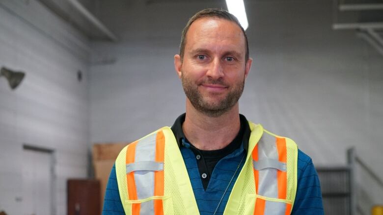 A middle-aged man wearing a blue shirt and safety vest.