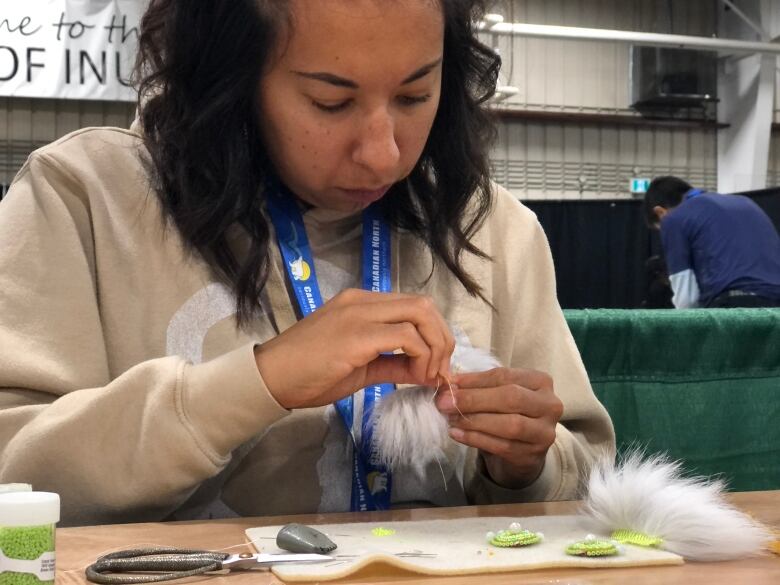 A woman sews fur and beads together.