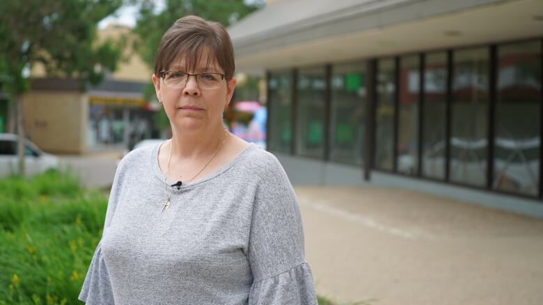 A portrait of a woman with glasses in a grey shirt outside of a building in Brandon, Manitoba. 