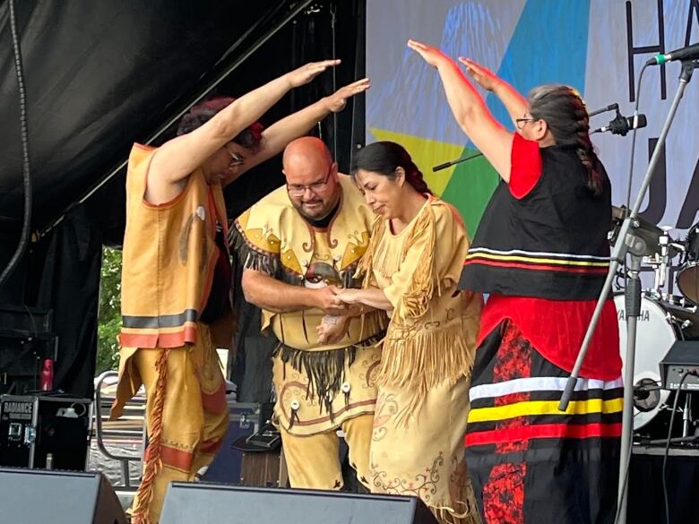 Four Indigenous Dancers, wearing Indigenous costumes, dance on stage.