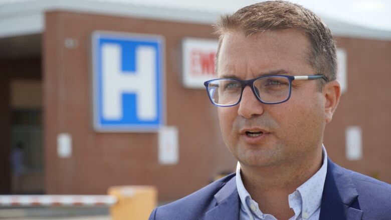 A man in a suit speaks outside a hospital.