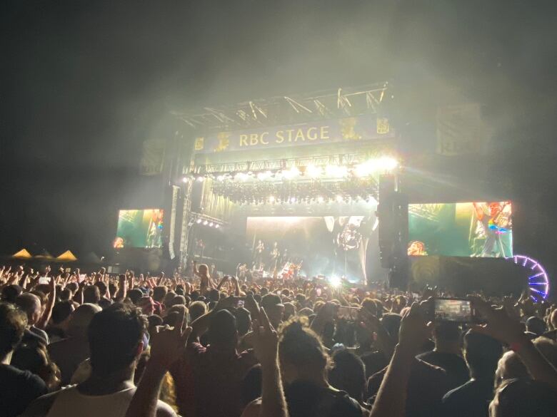 A large crowd of people raise their hands toward a stage where a band plays music.