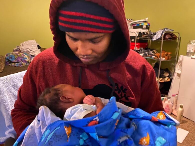 A man in a hooded sweatshirt holds a baby.