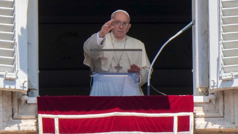 A man in white robes waves from a window. 