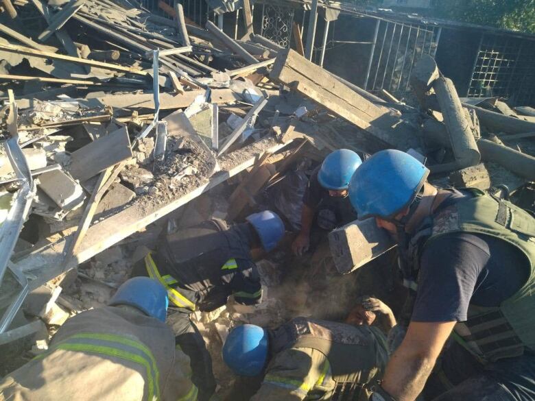 Five people, wearing light blue helmets, digging through piles of boards and rubble.