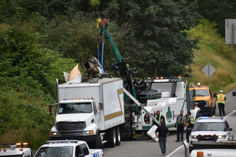 A tow truck and multiple police vehicles attend the scene of a cherry-picker truck that struck the Glover Road overpass on Highway 1 in Langley, B.C. on Monday. A long line of traffic is backed up in the lanes beside the incident.