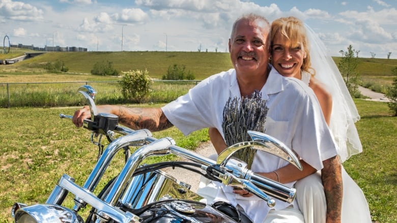 A man and a woman sit on a motorcycle in their wedding clothes. 