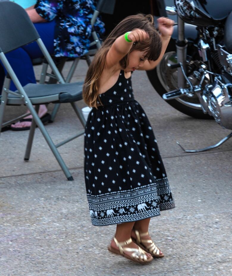 A small girl dances by herself on the pavement. 