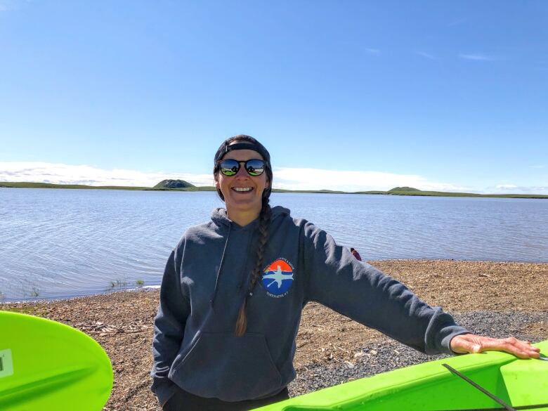 A woman smiles on a beach standing next to paddle equipment.