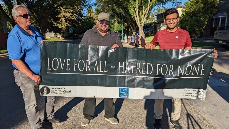 Three men hold up a sign that reads 