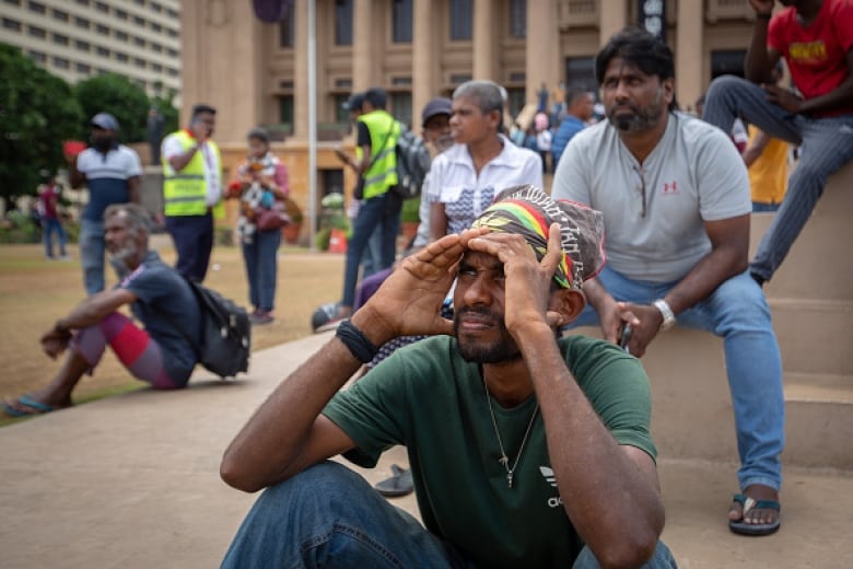 Men sit outside in a city, looking off-camera.