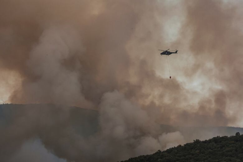 A helicopter is seen above a mountain, surrounded by smoke.