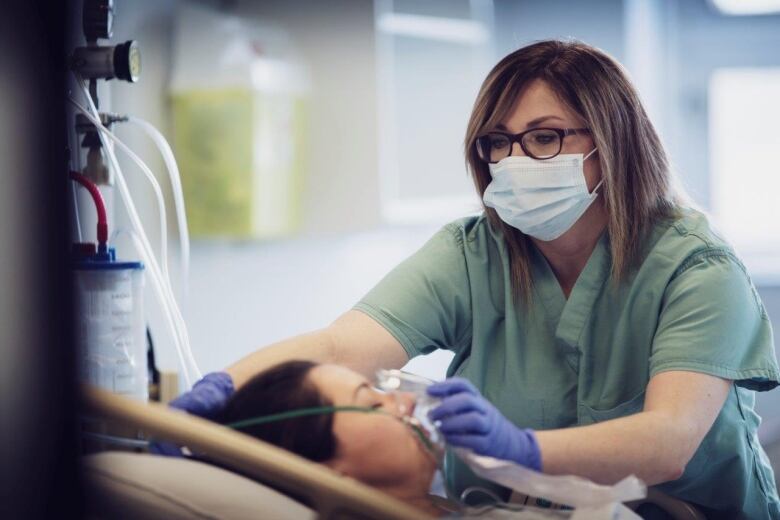 A nurse places an oxygen mask over a patient's face as the woman lies on a hospital bed. 