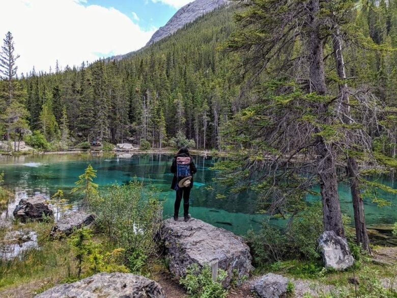 A woman stands near an isolated mountain lake. 