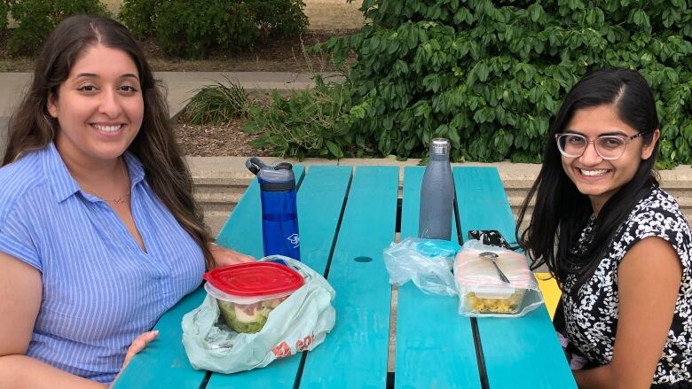 Two women sit on opposite sides of a picnic table that has yellow seats and a blue table top.