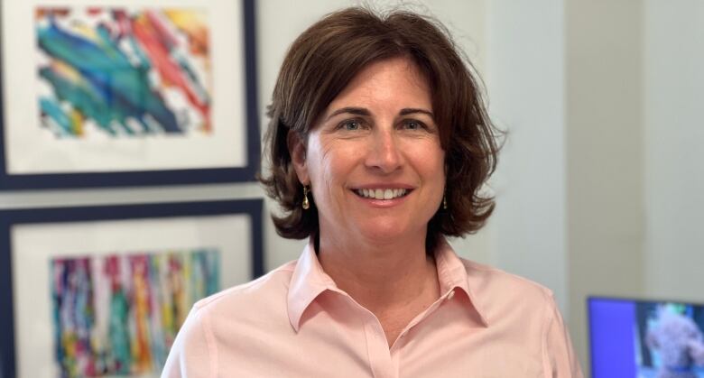 A smiling woman with brown hair wearing a pink shirt.