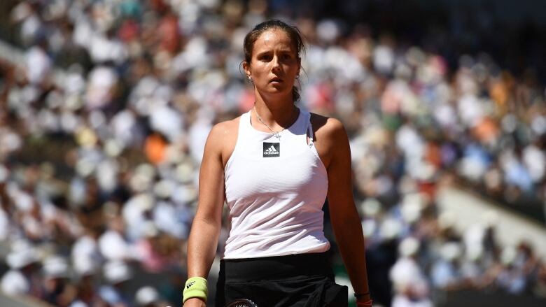 A woman walks with a tennis racket in her hand in front of a large crowd of people.