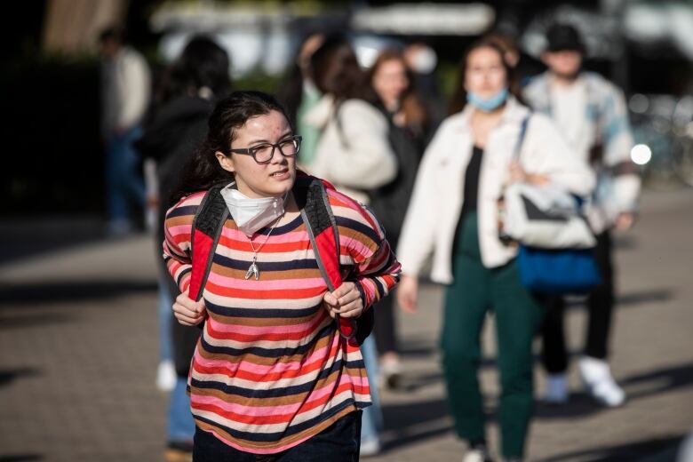 Students wearing backpacks and masks around their necks walk around a campus.