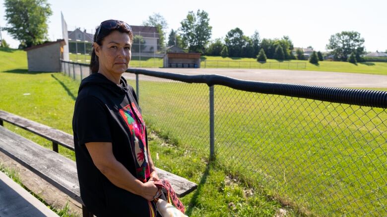 A woman is by a fence at a baseball diamond.