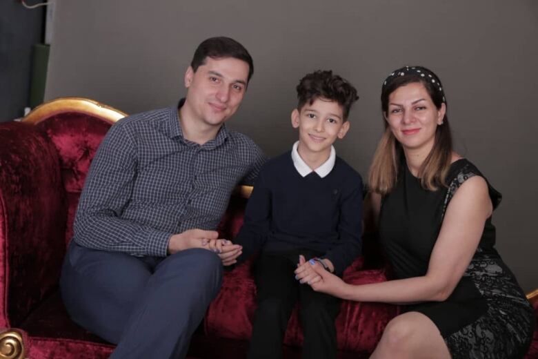 Sasan Ahmadiannamini sits facing the camera with his wife and child.