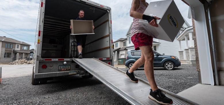 Man and woman carry boxes down a ramp out of a moving van. 