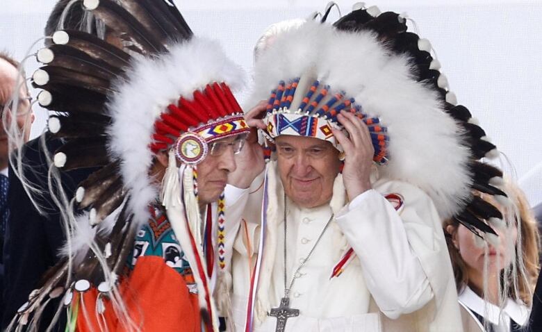 Two men (a Chief and the Pope) facing each other, each wearing a traditional headdress. 