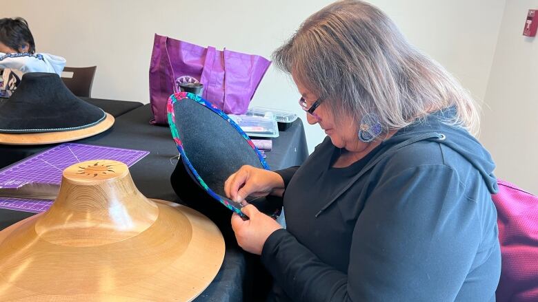 Thelma Sawyer sewing a colourful hat brim.