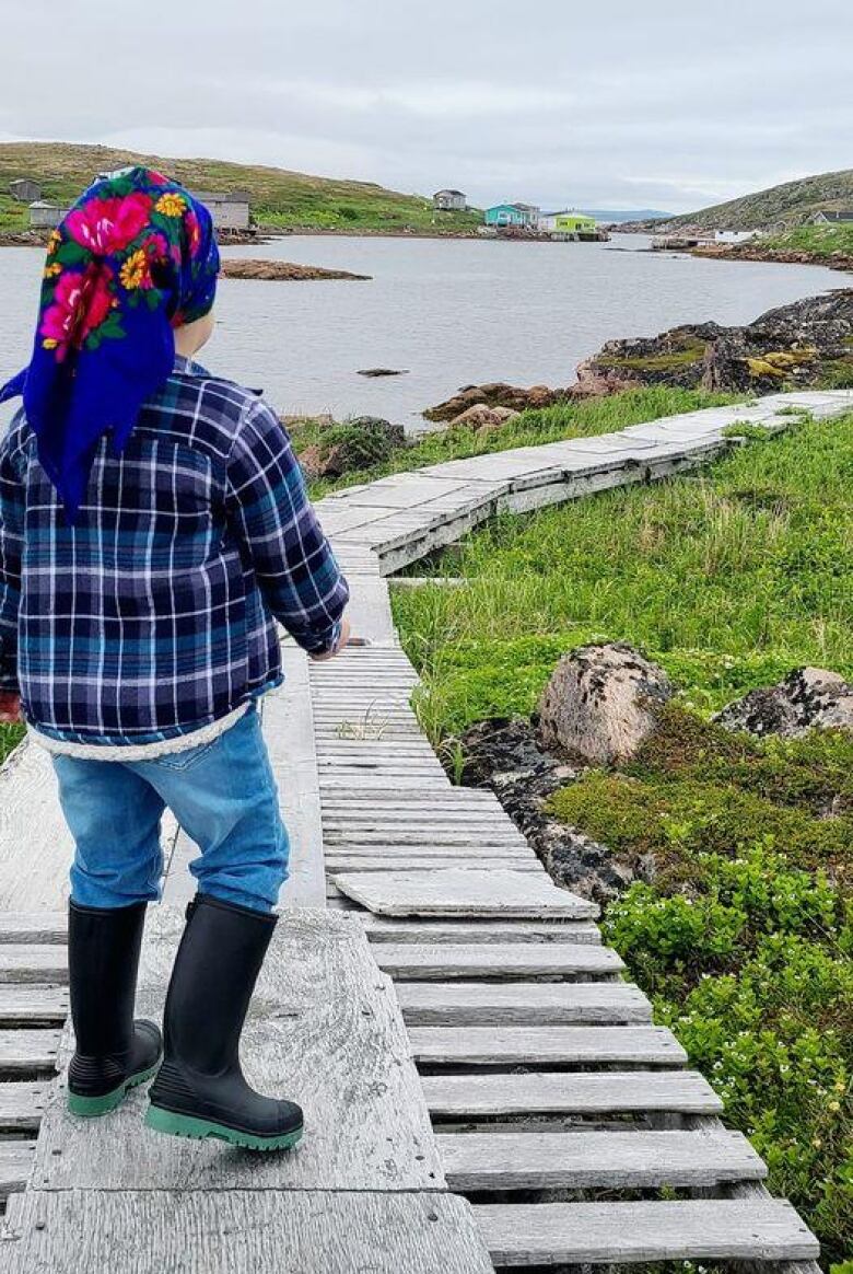 A young girl walks along a boardwalk by a lake.