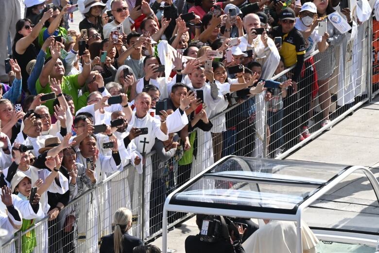 Clergy line fence holding cellphones as Pope passes.