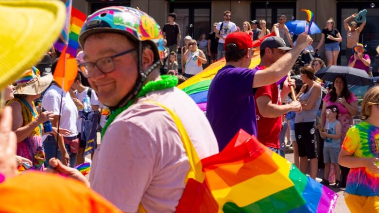 man with bike helmet with pink shirt and with Pride rainbow coloured bag over his shoulder