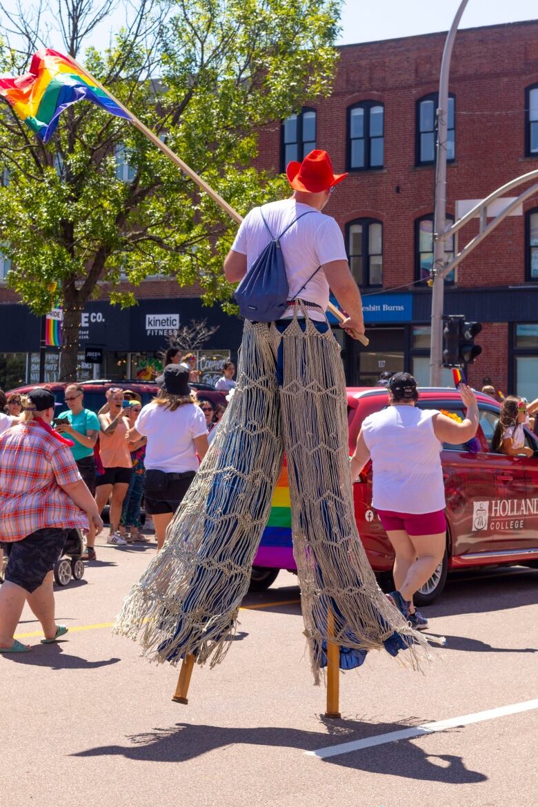 man on stilts carrying Pride rainbow flag