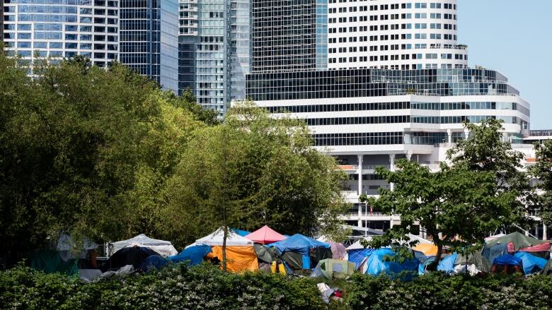 A number of tents at a waterfront park, in the shadow of large skyscrapers.